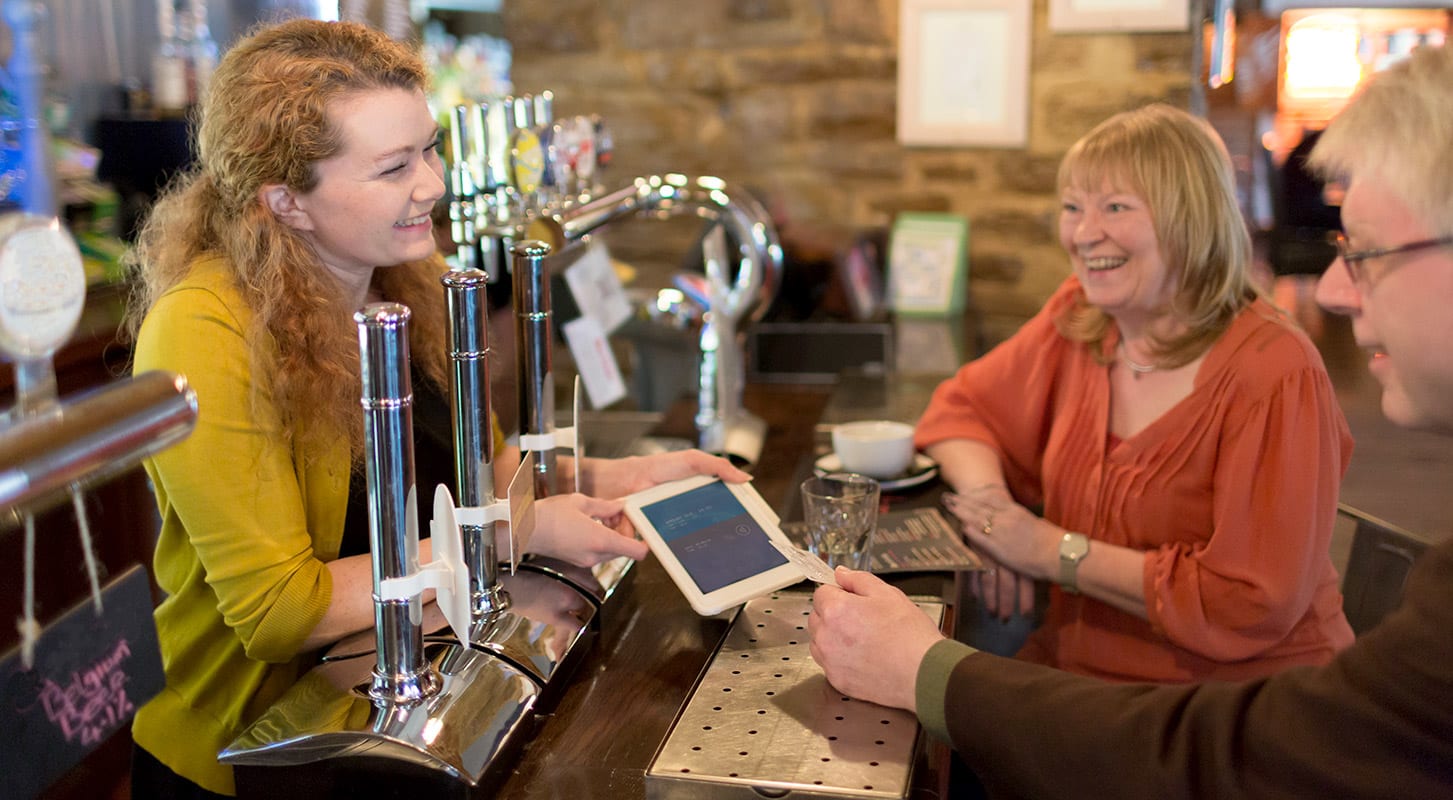 A woman and a man engage in conversation at a bar, with a female bartender attending to them.